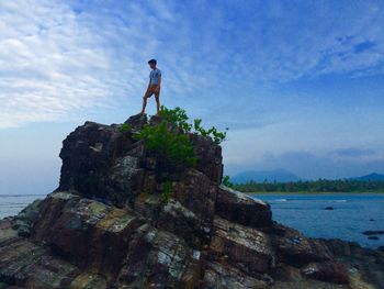 Low angle view of boy standing on rock formation against sky