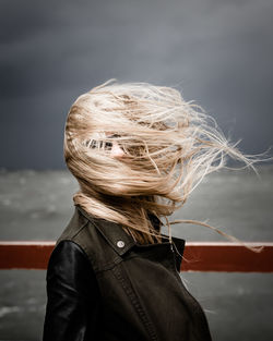 Woman with obscured face standing by railing against cloudy sky