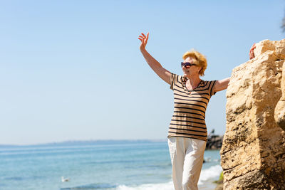 Elderly attractive smiling woman standing on a rock on the seashore