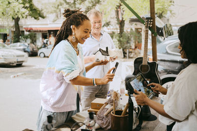 Happy female customer paying while holding house model near stall at flea market