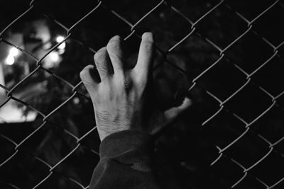 Cropped image of man holding chainlink fence