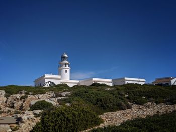 Lighthouse by building against clear blue sky