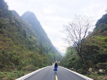 Man on road amidst trees against sky