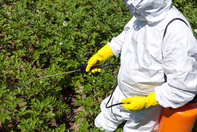 Midsection of man spraying pesticides on plants