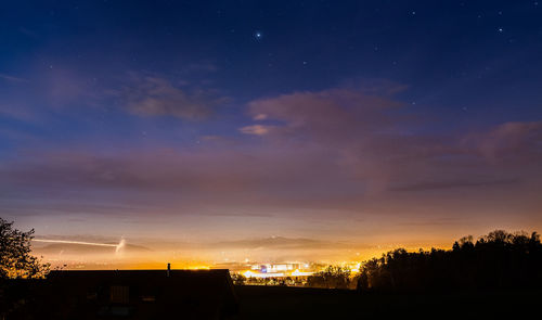 Silhouette trees and buildings against sky at night