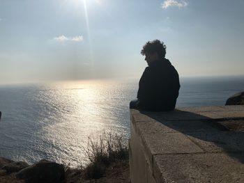 Rear view of boy sitting by sea against sky