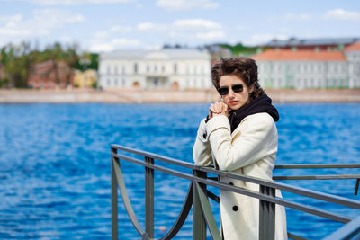 Beautiful young woman walks along embankment in white coat and black sweatshirt