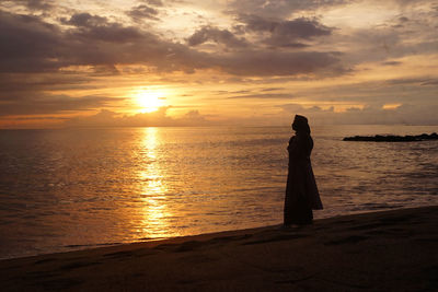 Silhouette woman standing at beach against sky during sunset