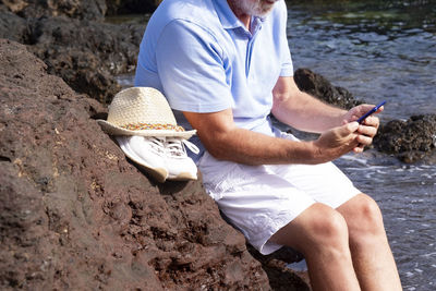 Midsection of man holding mobile phone while sitting on beach