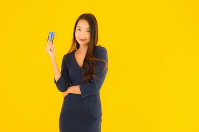 Young woman standing against yellow background