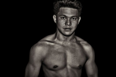Portrait of shirtless muscular male model standing against black background