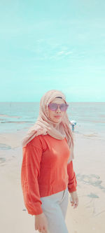 Young woman standing at beach against sky