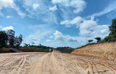 Dirt road amidst field against sky