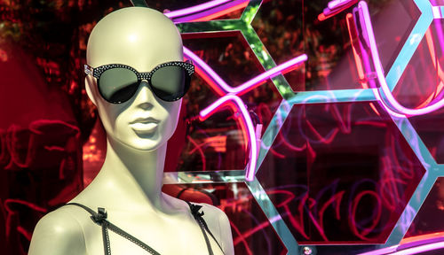 Digital composite image of mannequin wearing sunglasses against illuminated wall