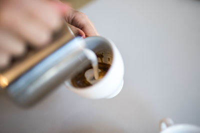 Close-up of hand pouring milk in coffee