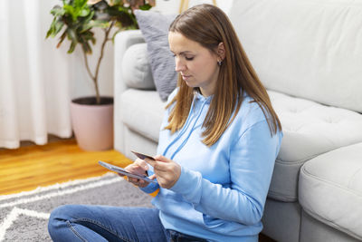 Young woman using mobile phone while sitting on bed at home