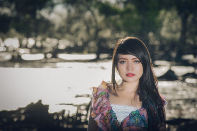 Portrait of young woman standing against lake in forest
