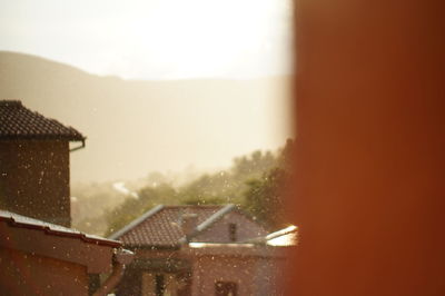 Buildings against sky seen through wet window