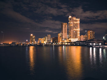 Illuminated city by sea against sky at night