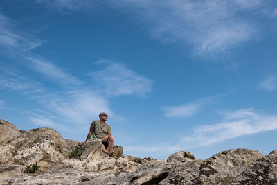 Low angle view of man sitting on rocks against sky