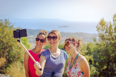 Smiling friends taking selfie with mobile phone against sky