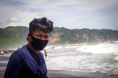 Portrait of a man standing on the beach, wearing a mask
