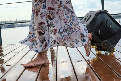 Low section of woman with suitcase walking on wet footpath