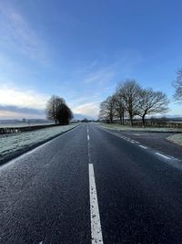 Empty road by bare trees against sky