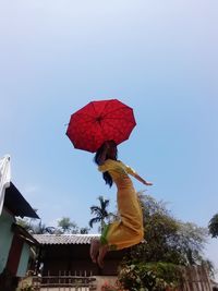 Low angle view of woman holding umbrella against clear sky