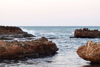 Scenic view of sea and rocks against clear sky