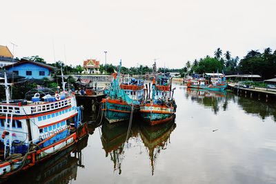 Fishing boats moored in river by buildings against sky