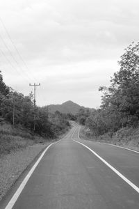 Empty road by trees against sky