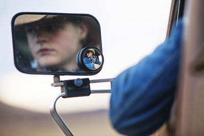 Reflection of teenage cowboy on side-view mirror of vehicle