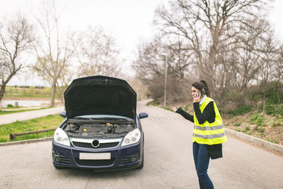 Young caucasian woman, talking on her cell phone while her car is broken down on the road.