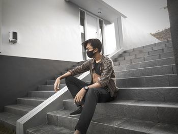 Young man wearing mask sitting on staircase outdoors