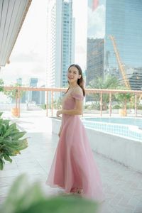Portrait of beautiful young woman wearing evening gown while standing by swimming pool against buildings