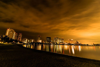 Illuminated buildings by sea against sky at night