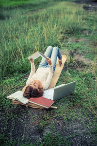 High angle view of young woman reading book while lying on field