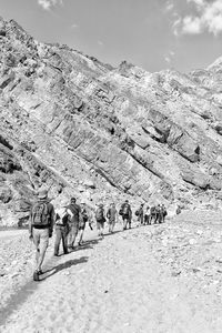 People walking against rock formation during sunny day