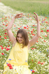 A beautiful young blonde woman in a yellow dress stands among a flowering field