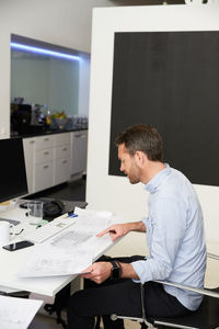 Side view of architect analyzing blueprints at desk in creative office