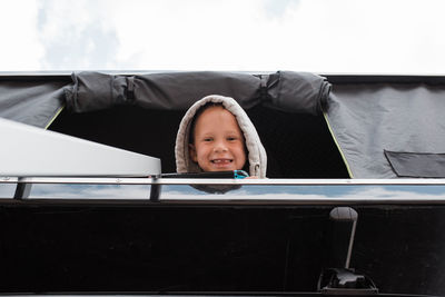 Boy smiling from roof top tent whilst camping