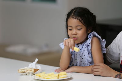 Cute daughter having meal while sitting by mother at home