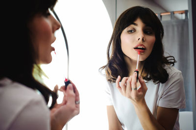 Close-up of young woman applying red lipstick in front of mirror at home