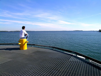 Rear view of man sitting on seat at pier over sea against sky