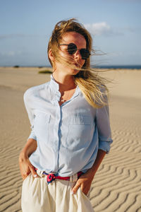 Young woman looking away while standing on sand at desert against sky