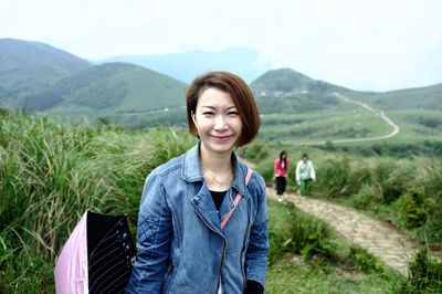 Portrait of young woman standing on field against mountains