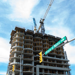 Low angle view of crane by building against sky