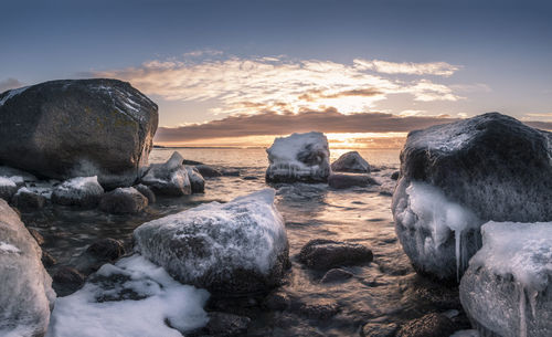 Rocks by sea against sky during sunset