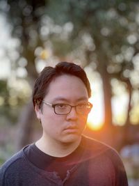 Portrait of young man in eyeglasses against trees and setting sun.